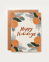 A holiday greeting card with a copper envelope behind it, featuring the words “Happy Holidays” in brown script and surrounded by illustrated citrus slices, green leaves, and blue-gray pine needles 