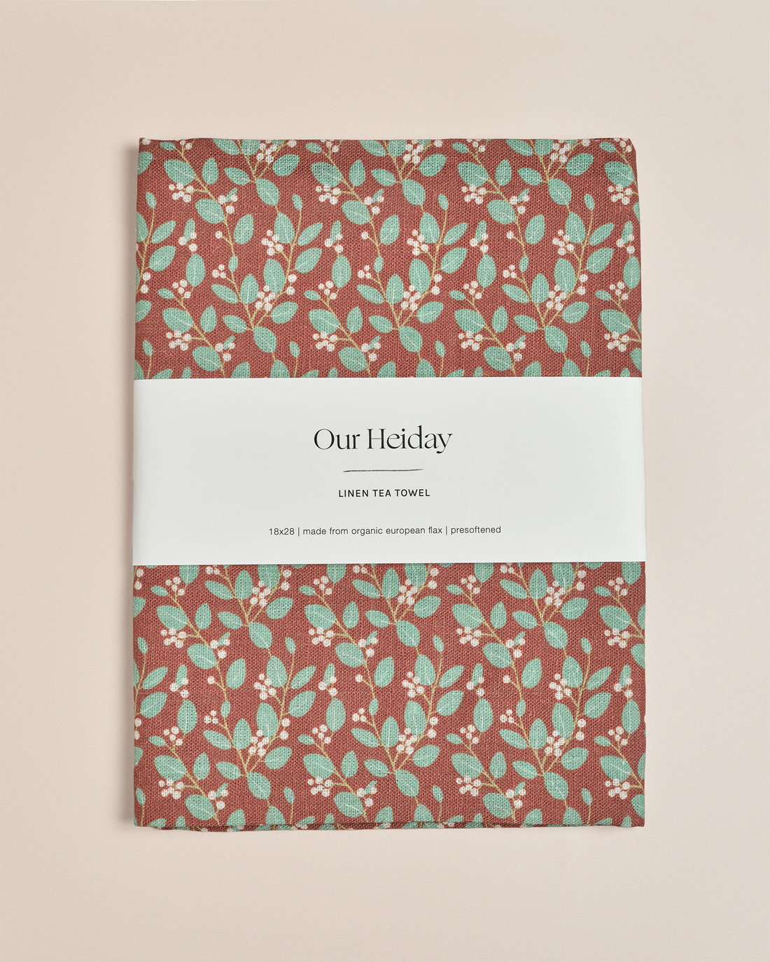 A rectangular linen tea towel with a rust-brown background and a repeating pattern of mint green leaves and small white berries,&