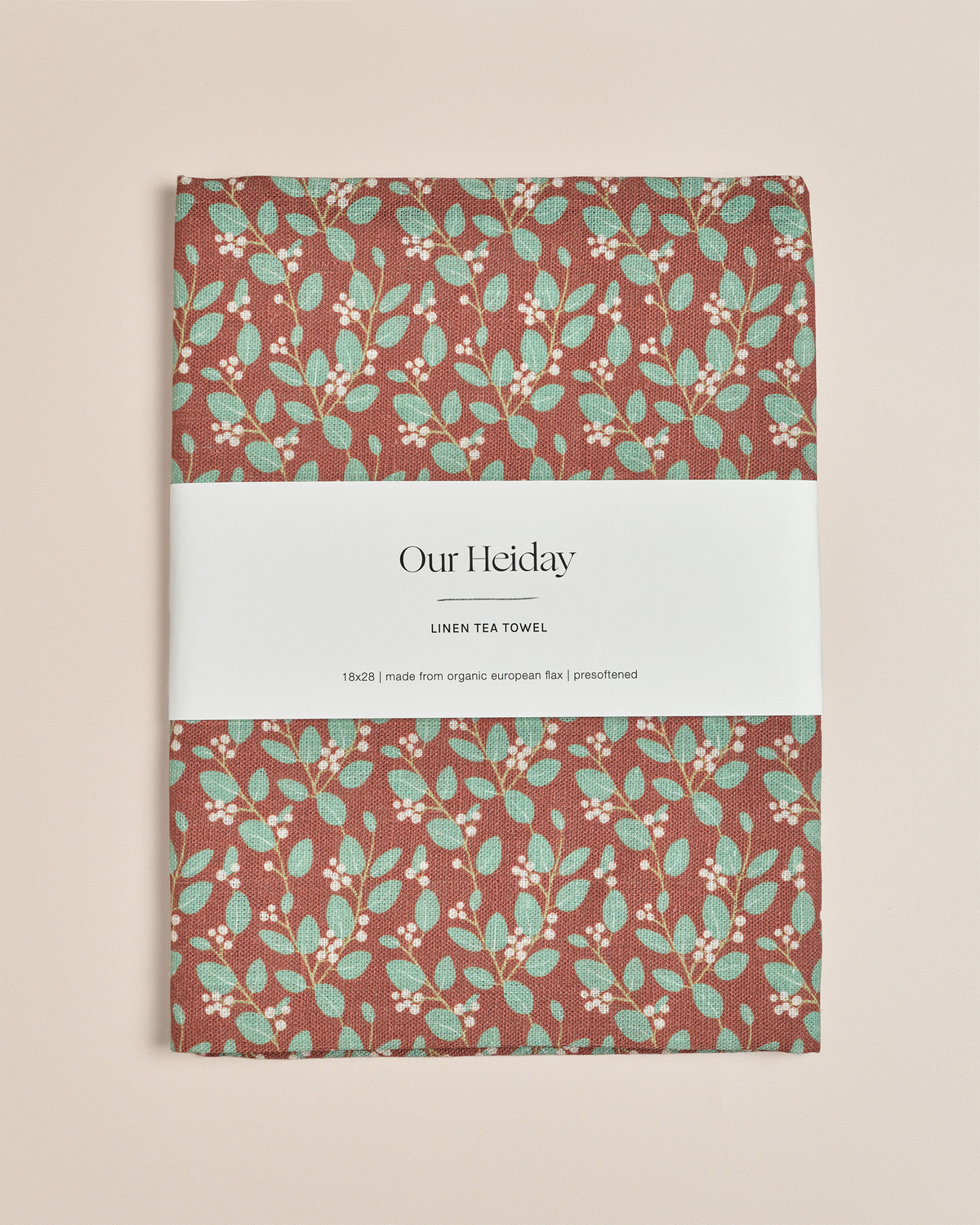 A rectangular linen tea towel with a rust-brown background and a repeating pattern of mint green leaves and small white berries,&