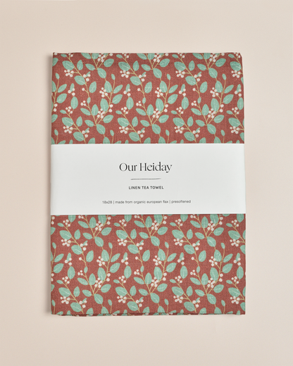 A rectangular linen tea towel with a rust-brown background and a repeating pattern of mint green leaves and small white berries,&
