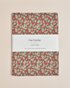 A rectangular linen tea towel with a rust-brown background and a repeating pattern of mint green leaves and small white berries,&